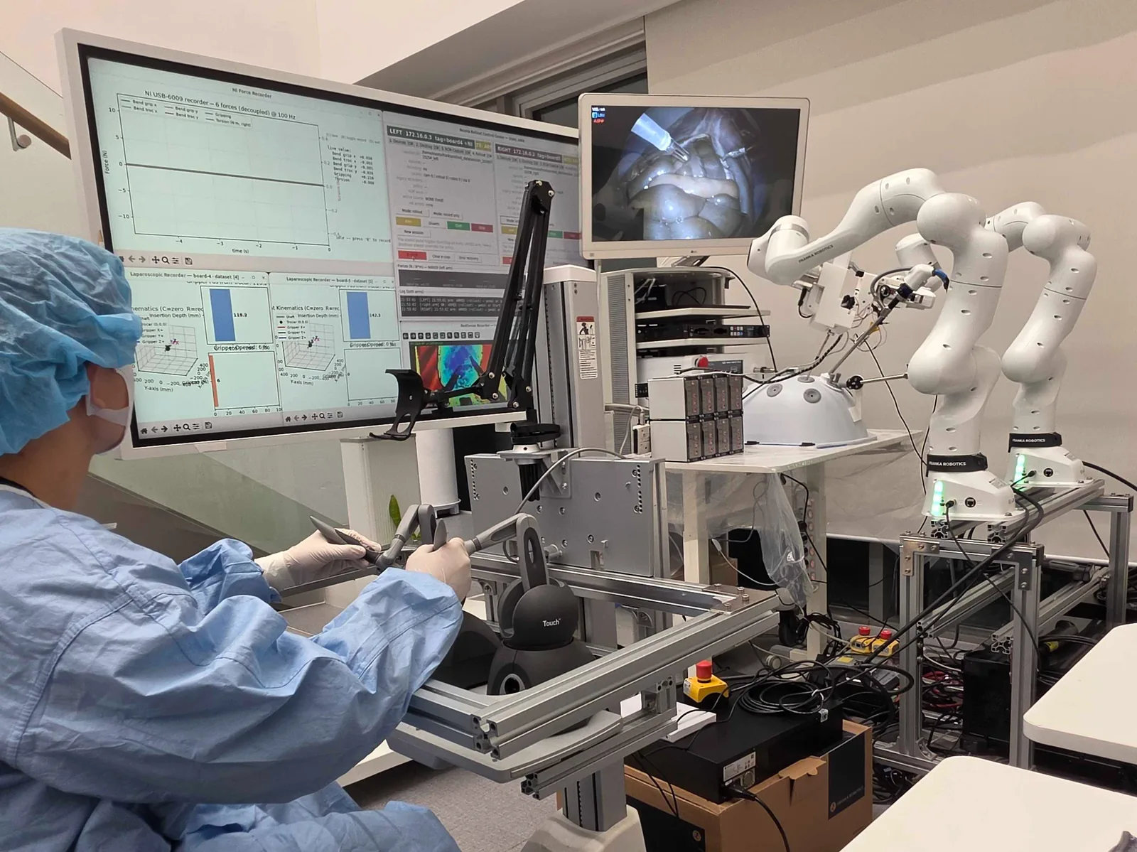 The two-FR3 ex-vivo rig: a surgeon at the phase keypress, monitors, and two arms holding instruments through a laparoscopic phantom